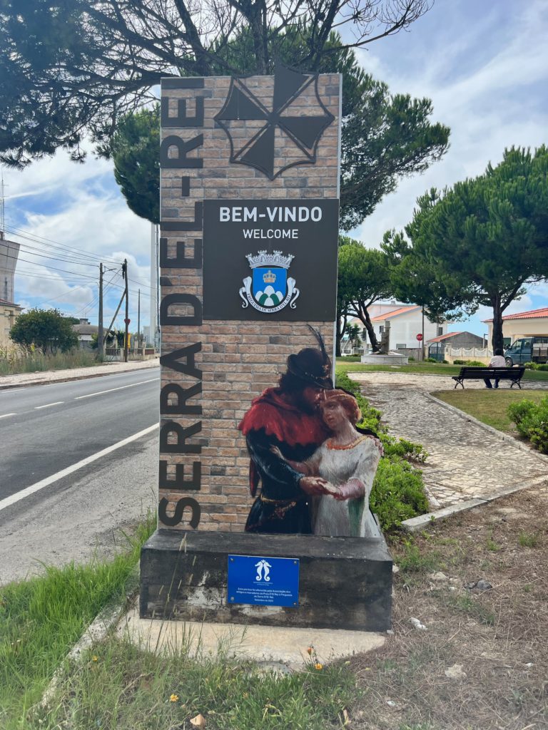 Tall brick welcome sign for Serra D'El Rei with Pedro and Inês  embracing each other at the bottom